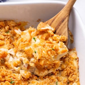 A wooden spoon lifting a serving of million dollar chicken casserole from a baking dish.