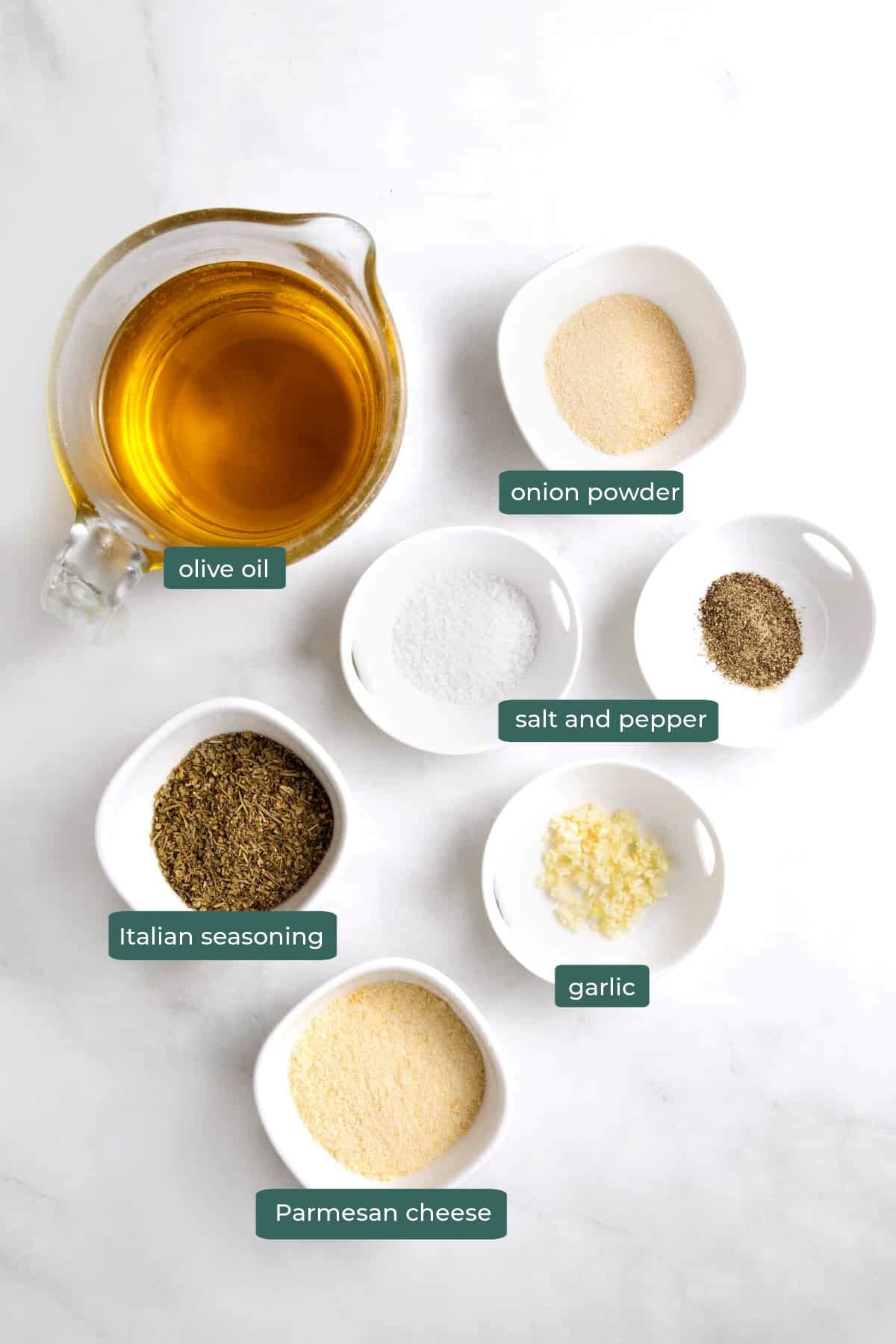 All of the ingredients for olive oil bread dip in bowls on a white countertop.