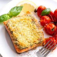 Pesto crusted salmon on a plate with roasted tomatoes.