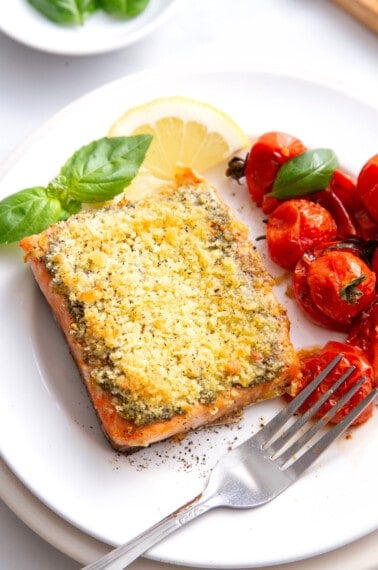 Pesto crusted salmon on a plate with roasted tomatoes.
