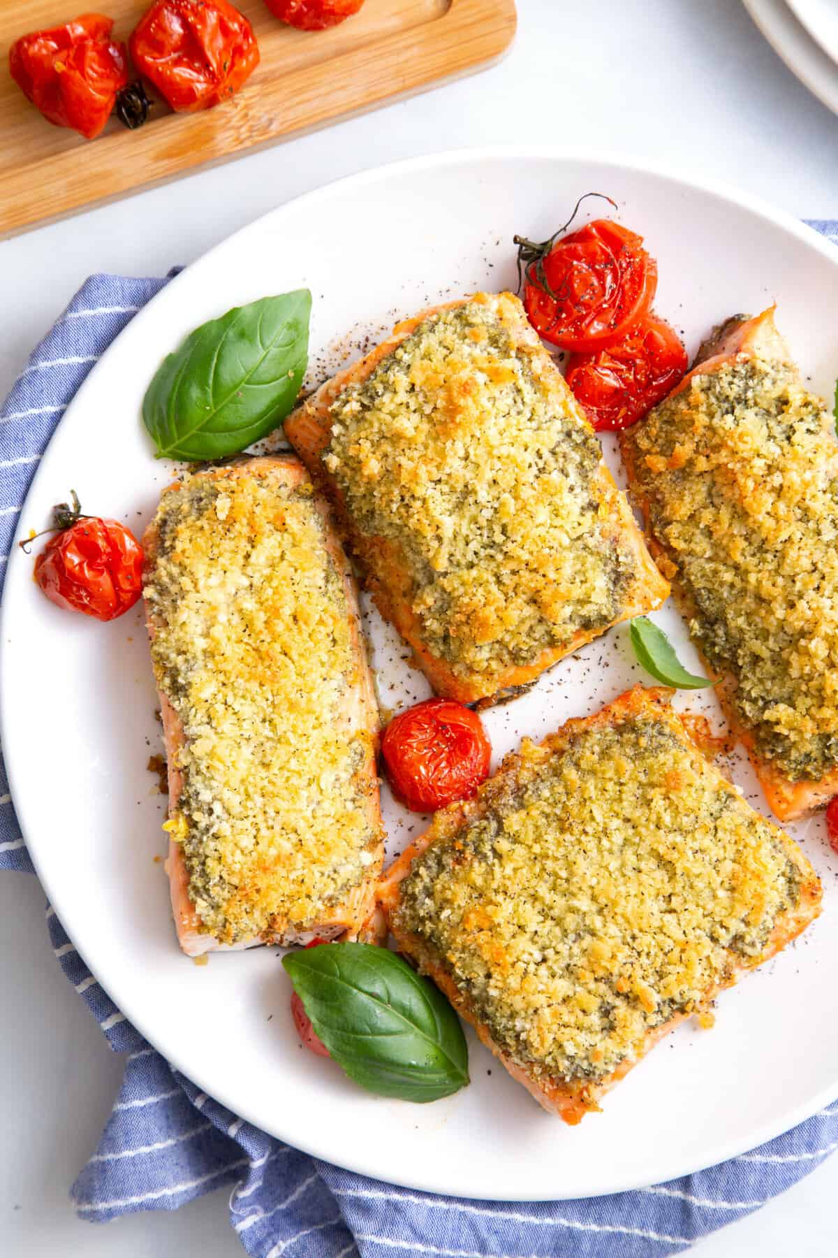 top down image of a plate of four panko pesto crusted salmon garnished with roasted tomatoes and fresh basil