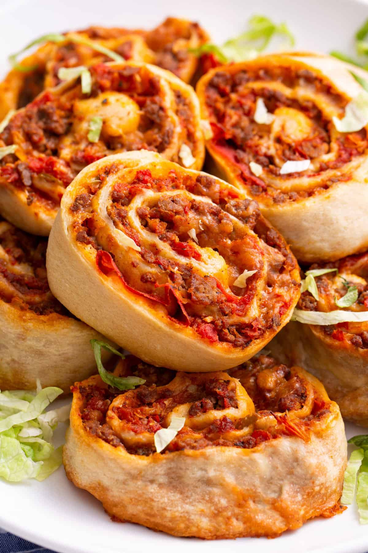 close up image of a pile of taco pinwheels served on a white round plate