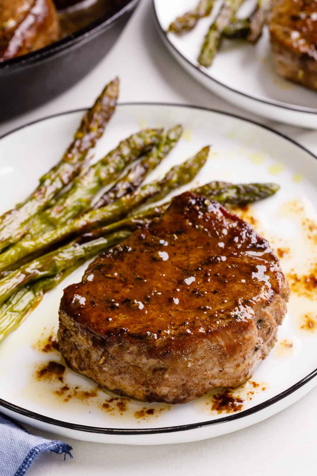 plate of filet mignon cooked in a cast iron skillet served on a white round plate with a side of roasted asparagus