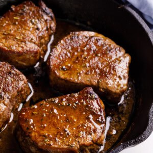 A cast iron skillet with four filet mignon steaks.