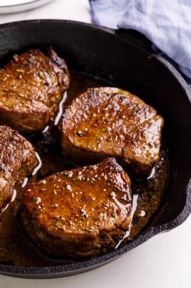 A cast iron skillet with four filet mignon steaks.