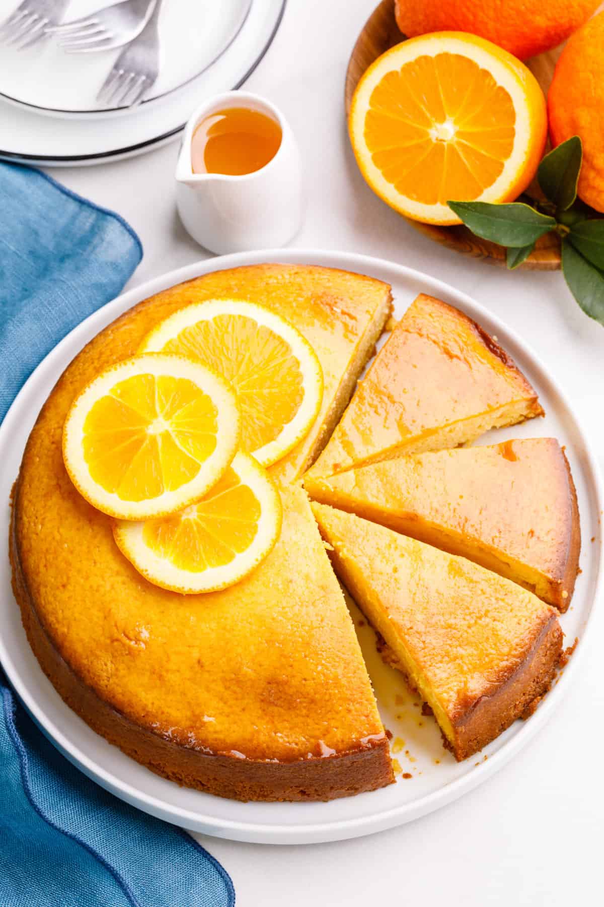 orange cake with three slices cut served on a white round plate topped with orange glaze and fresh orange slices