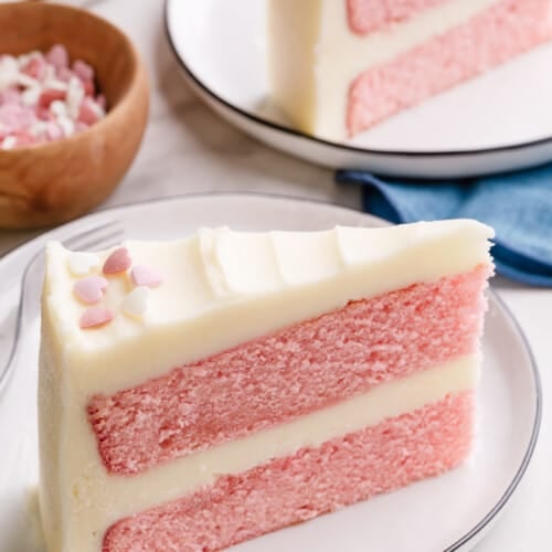 A slice of double layer pink velvet cake with buttercream frosting.