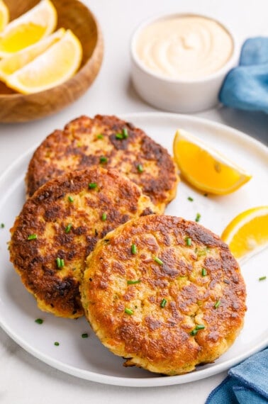 Three air fryer crab cakes on a plate with lemon wedges.