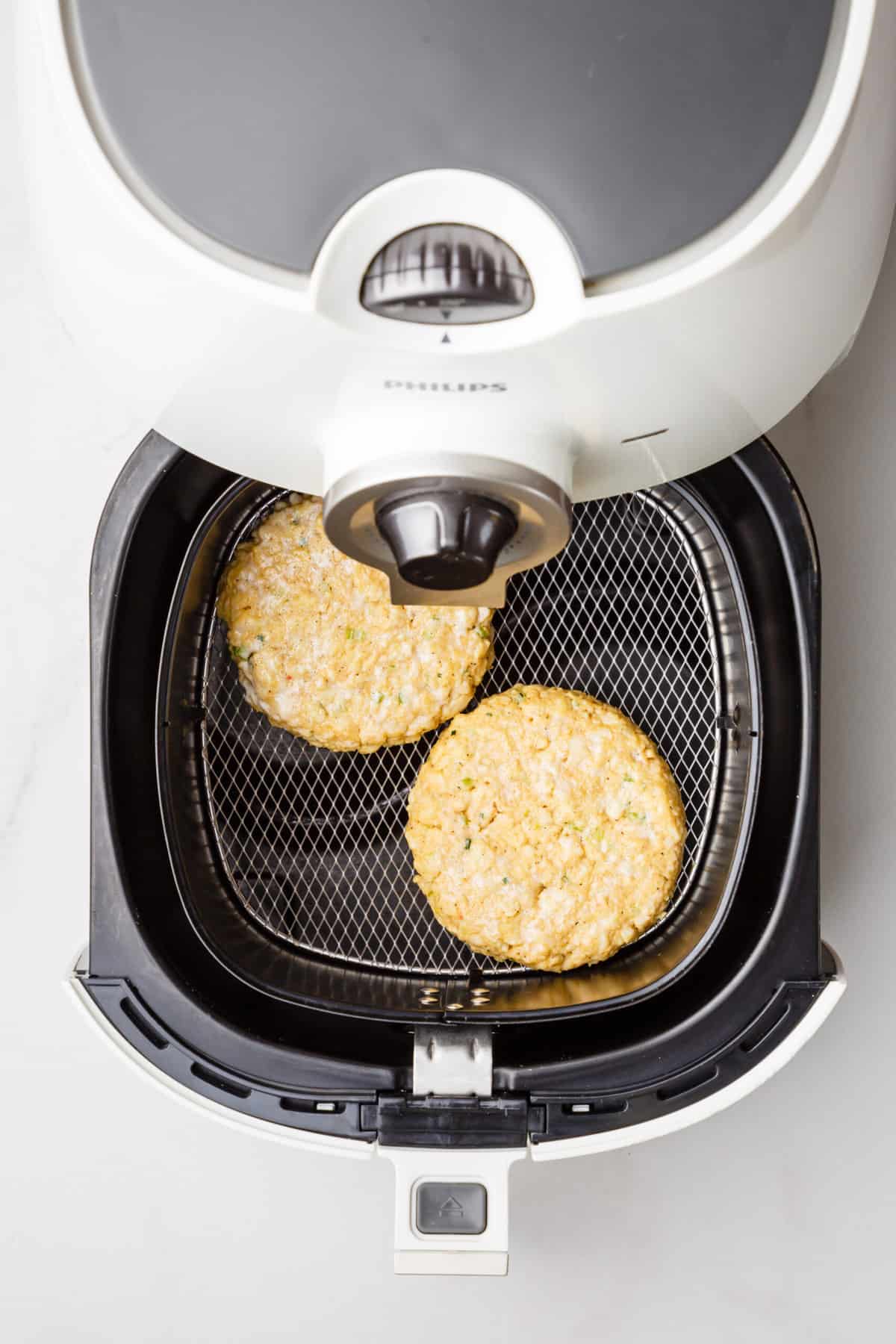 step 4 to make air fryer crab cakes, two crab cakes placed in an air fryer basket 