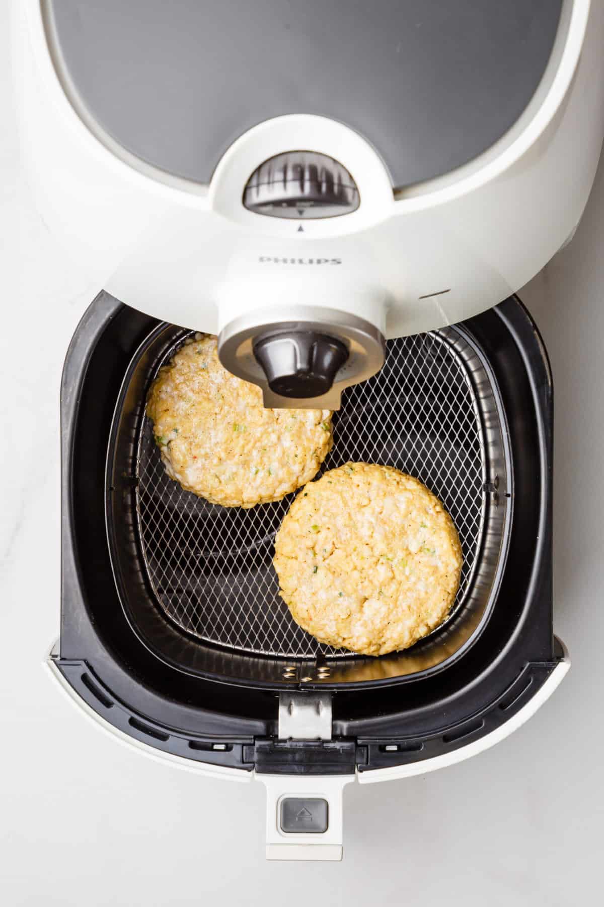 step 4 to make air fryer crab cakes, two crab cakes placed in an air fryer basket