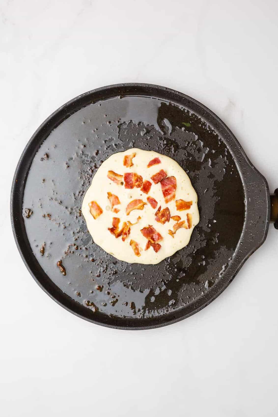 step 4 to make bacon pancakes, ladle down pancake batter in the same cast iron skillet and sprinkle the top with bacon