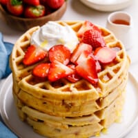 A stack of strawberry waffles topped with fresh strawberries and whipped cream.