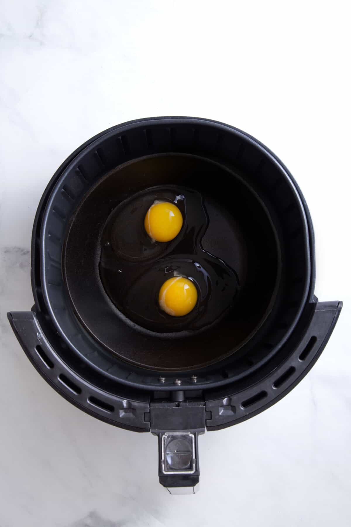 step 2 to make air fryer eggs, crack two eggs in an air fryer basket.