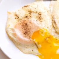 Two basted eggs on a plate with the yolk running.