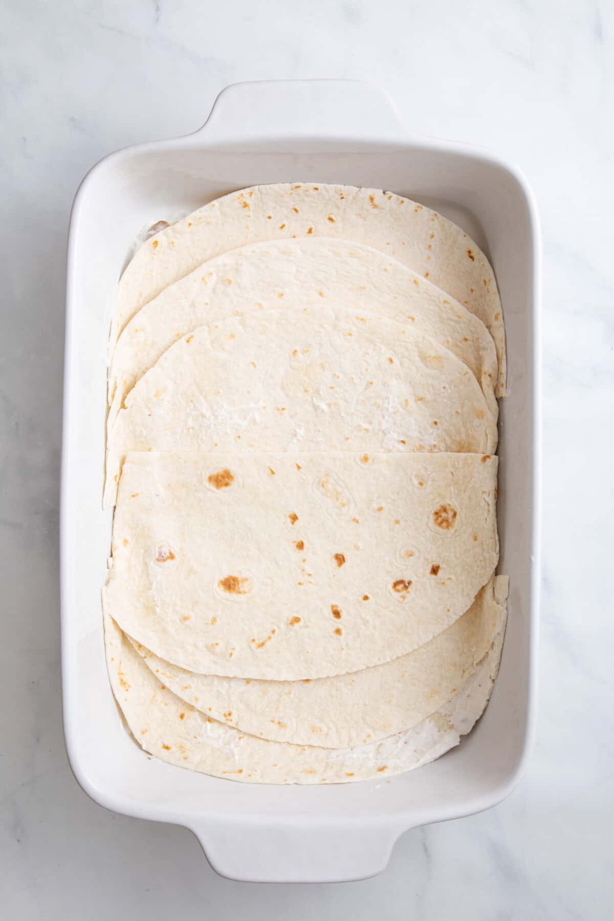 step 1 to make burrito casserole, layer tortillas at the bottom of a casserole dish.