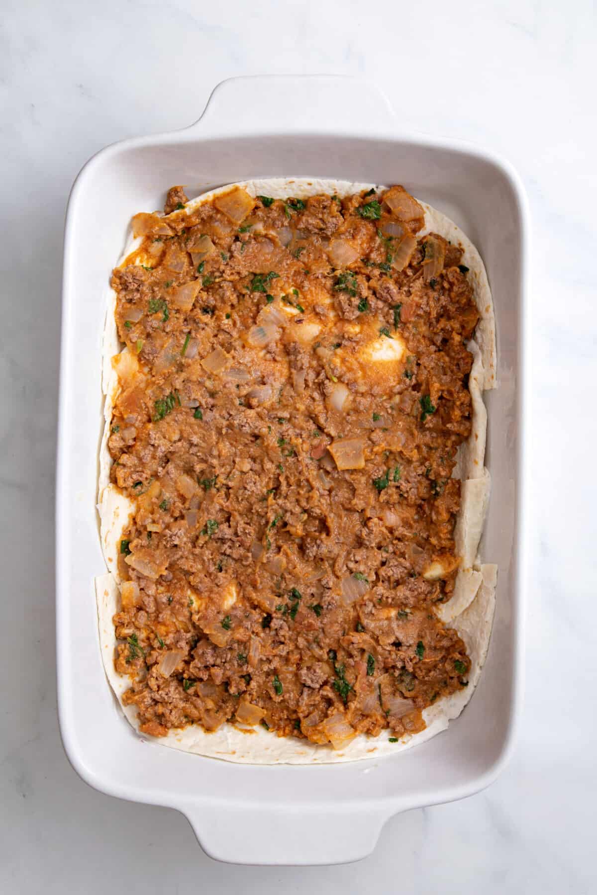 step 2 to make burrito casserole, spread ground beef mix on top of the tortillas.