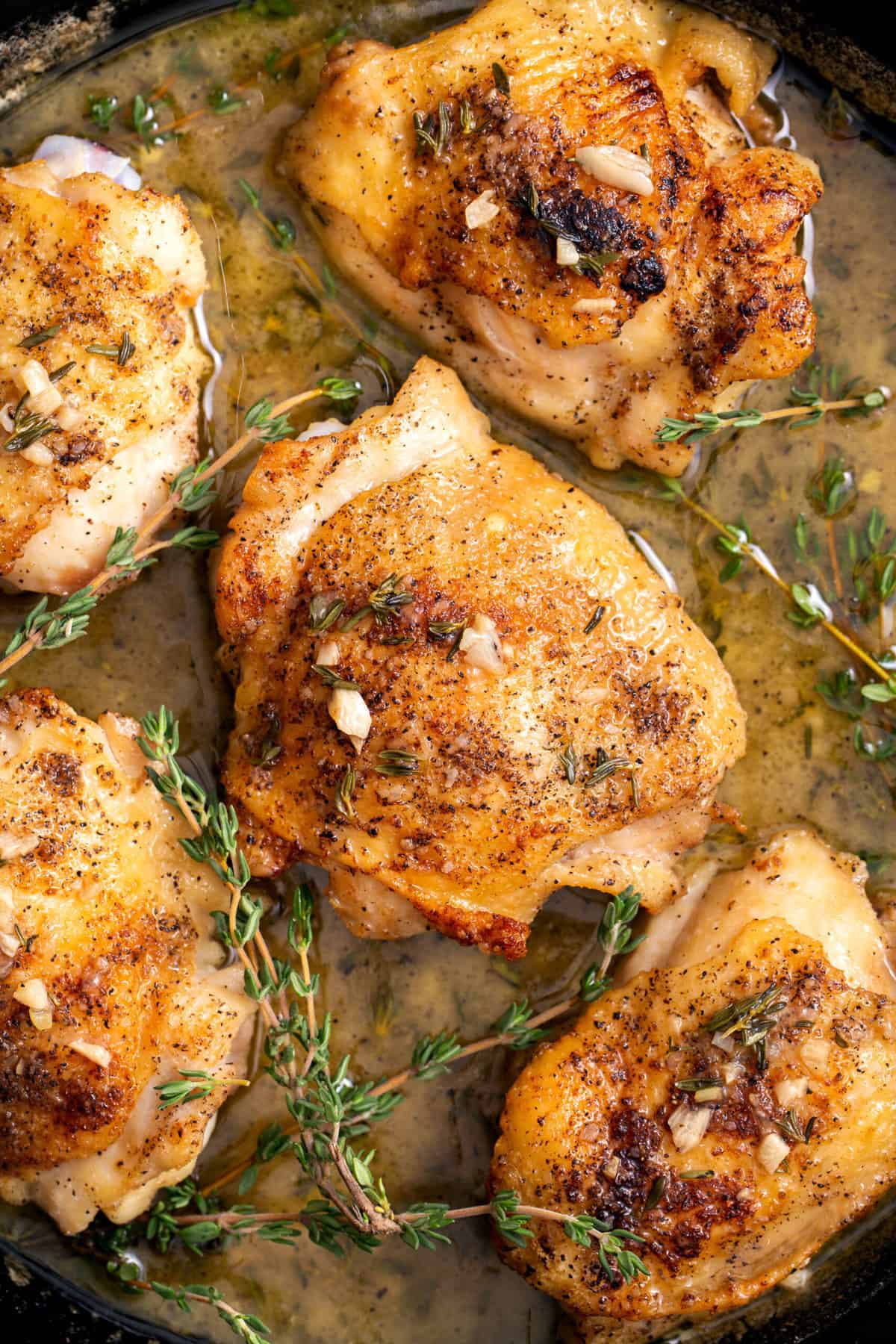 top down image of five chicken thighs sitting in a cast iron pan with fresh thyme