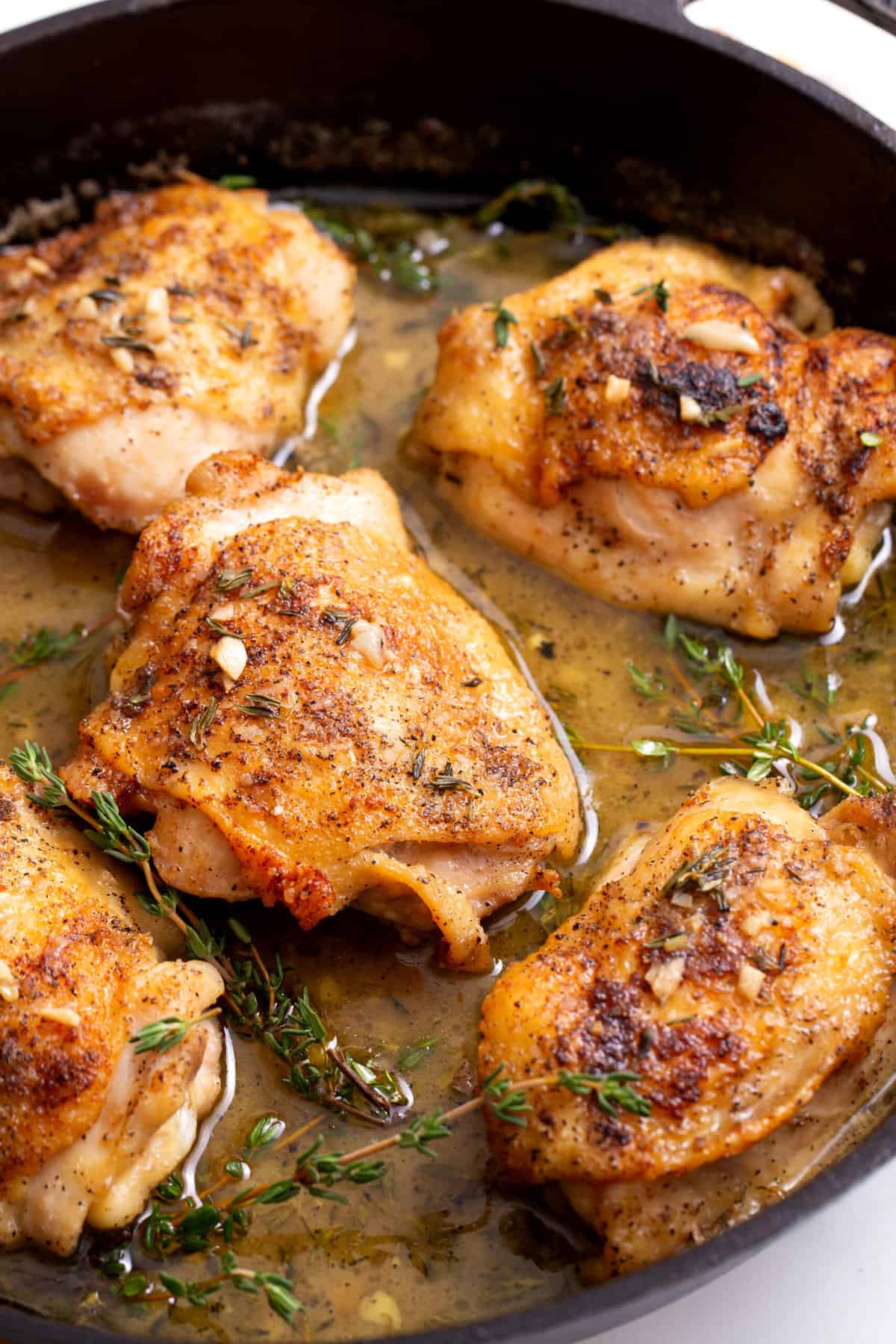 five chicken thighs in a cast iron skillet sitting in sauce and fresh thyme