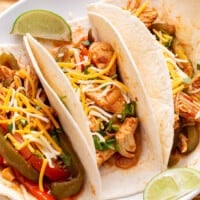 Three tortilla shells stuffed with crockpot chicken fajitas.