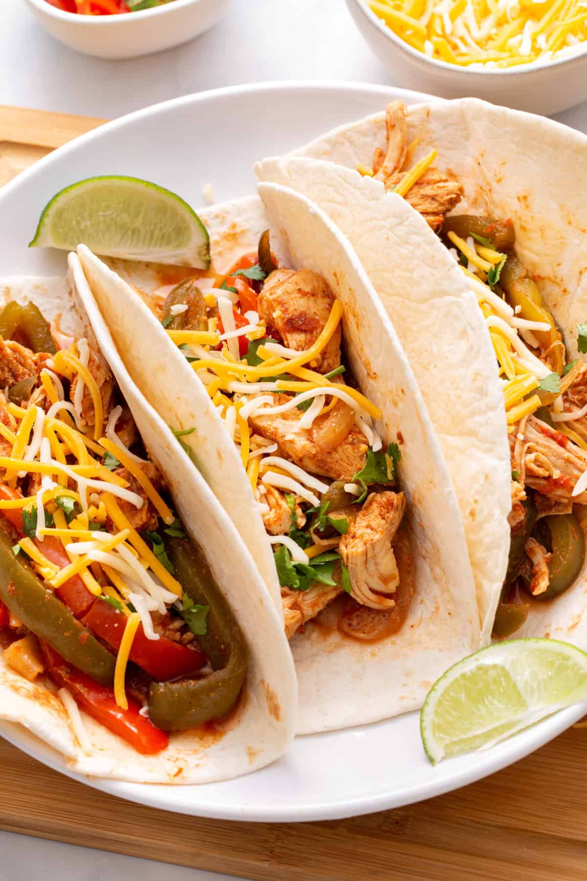 close up of three crock pot chicken fajita tacos served on a white round plate with a lime wedge.