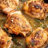 chicken thighs in a seasoned butter sauce in a cast iron skillet.