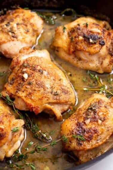 chicken thighs in a seasoned butter sauce in a cast iron skillet.