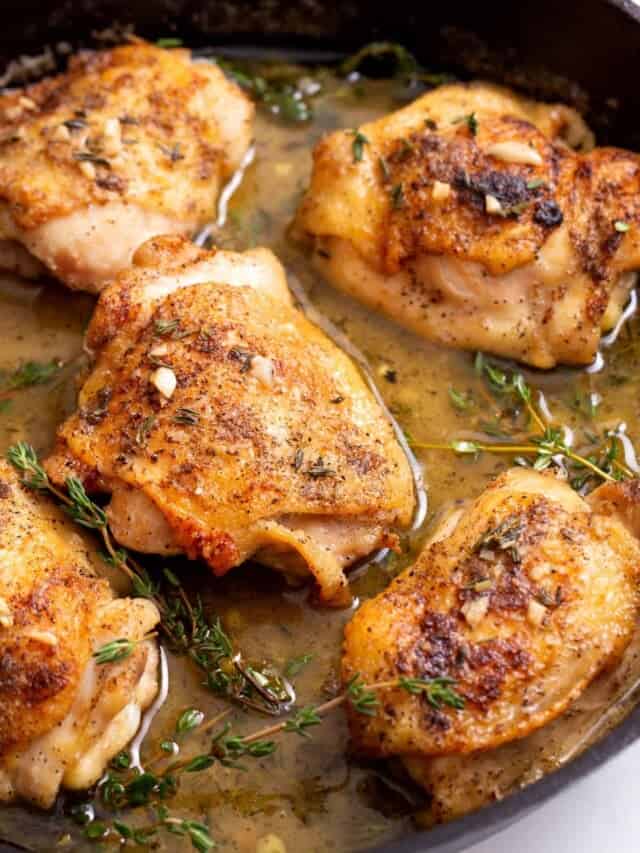 chicken thighs in a seasoned butter sauce in a cast iron skillet.