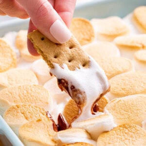 A graham cracker being dunked into s'mores dip.