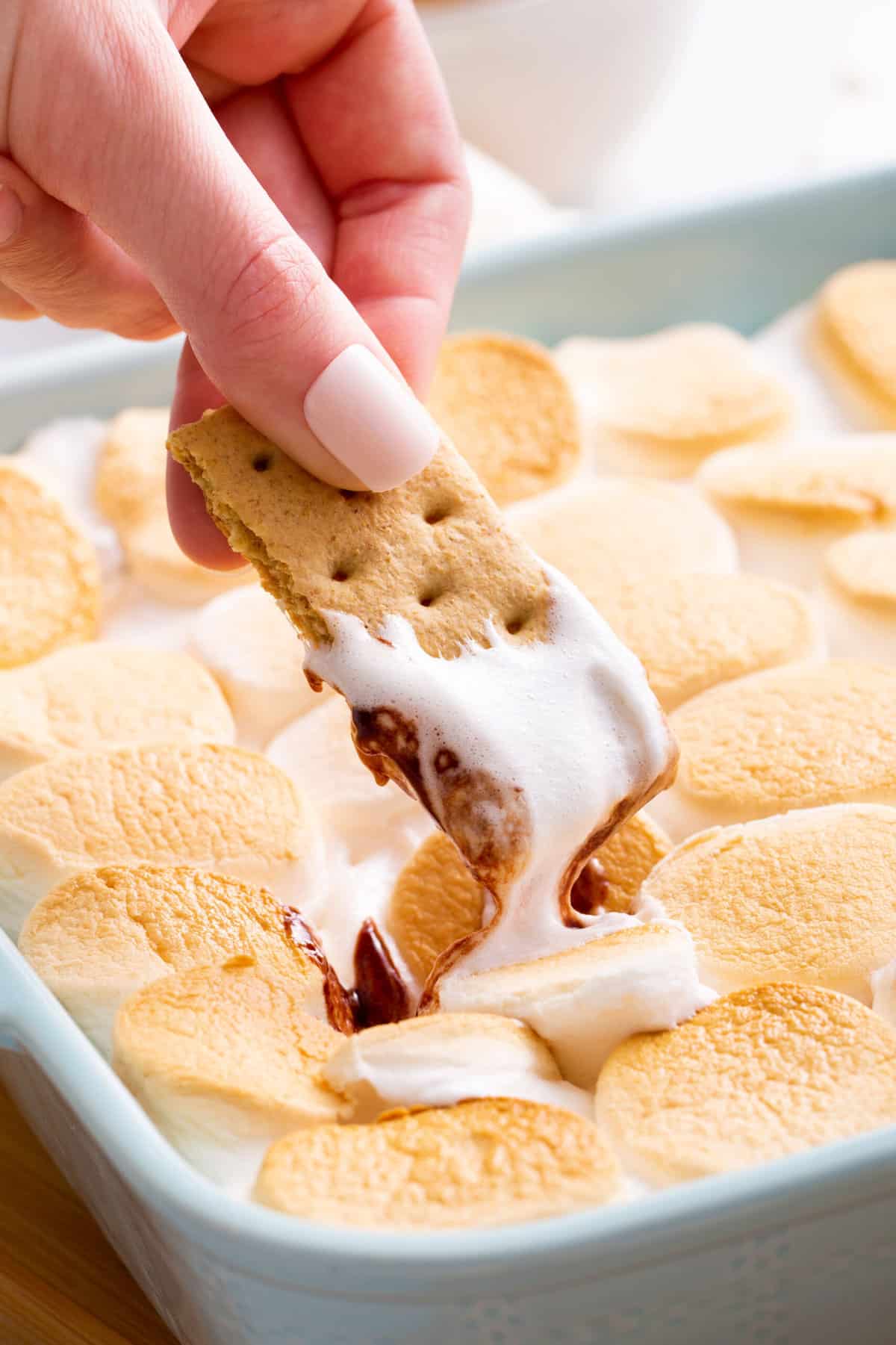 a graham cracker dipping into baked s'mores dip