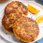 Three air fryer crab cakes on a plate with two lemon wedges.