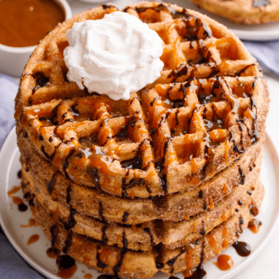 A stack of churro waffles topped with whipped cream and chocolate sauce.