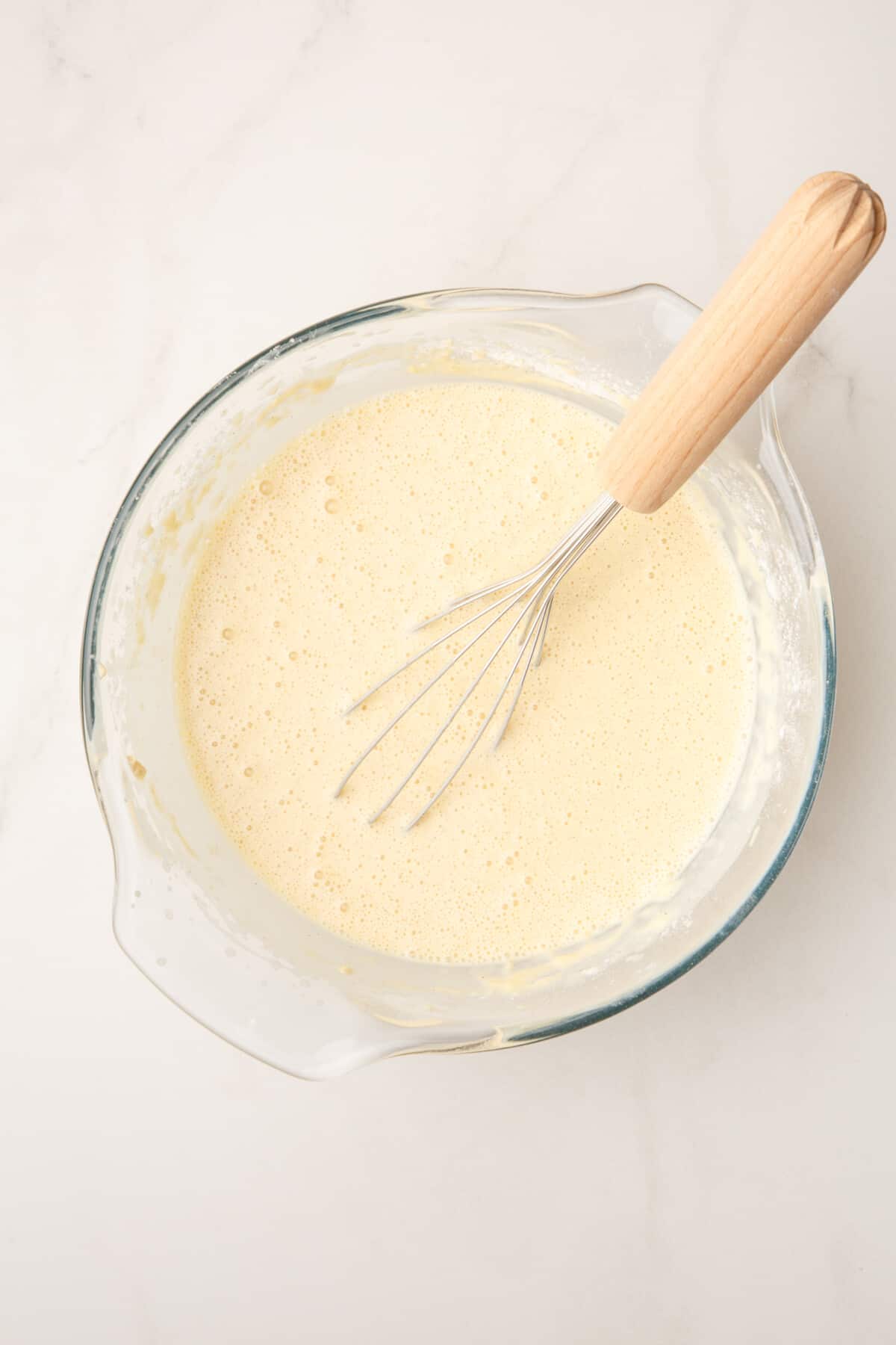 waffle batter in a large glass bowl with a whisk.