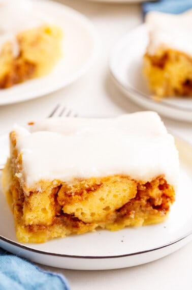 A slice of frosted cinnamon roll cake on a plate.