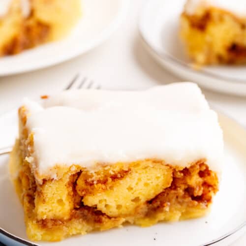 A slice of frosted cinnamon roll cake on a plate.