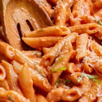 Creamy tomato pasta being stirred with a wooden spoon.