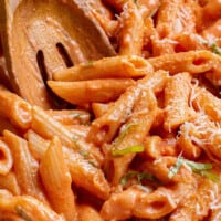 Creamy tomato pasta being stirred with a wooden spoon.