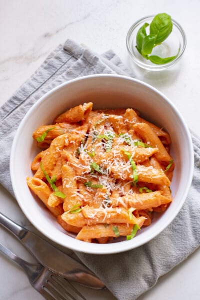 A bowl of creamy tomato pasta topped with melted cheese and parsley