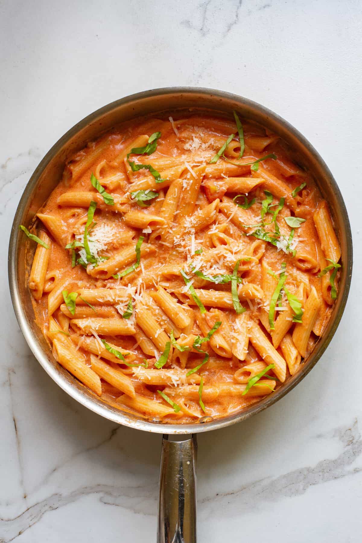 step 4 to make creamy tomato pasta, add in the cooked penne pasta and garnish with fresh basil and more cheese.