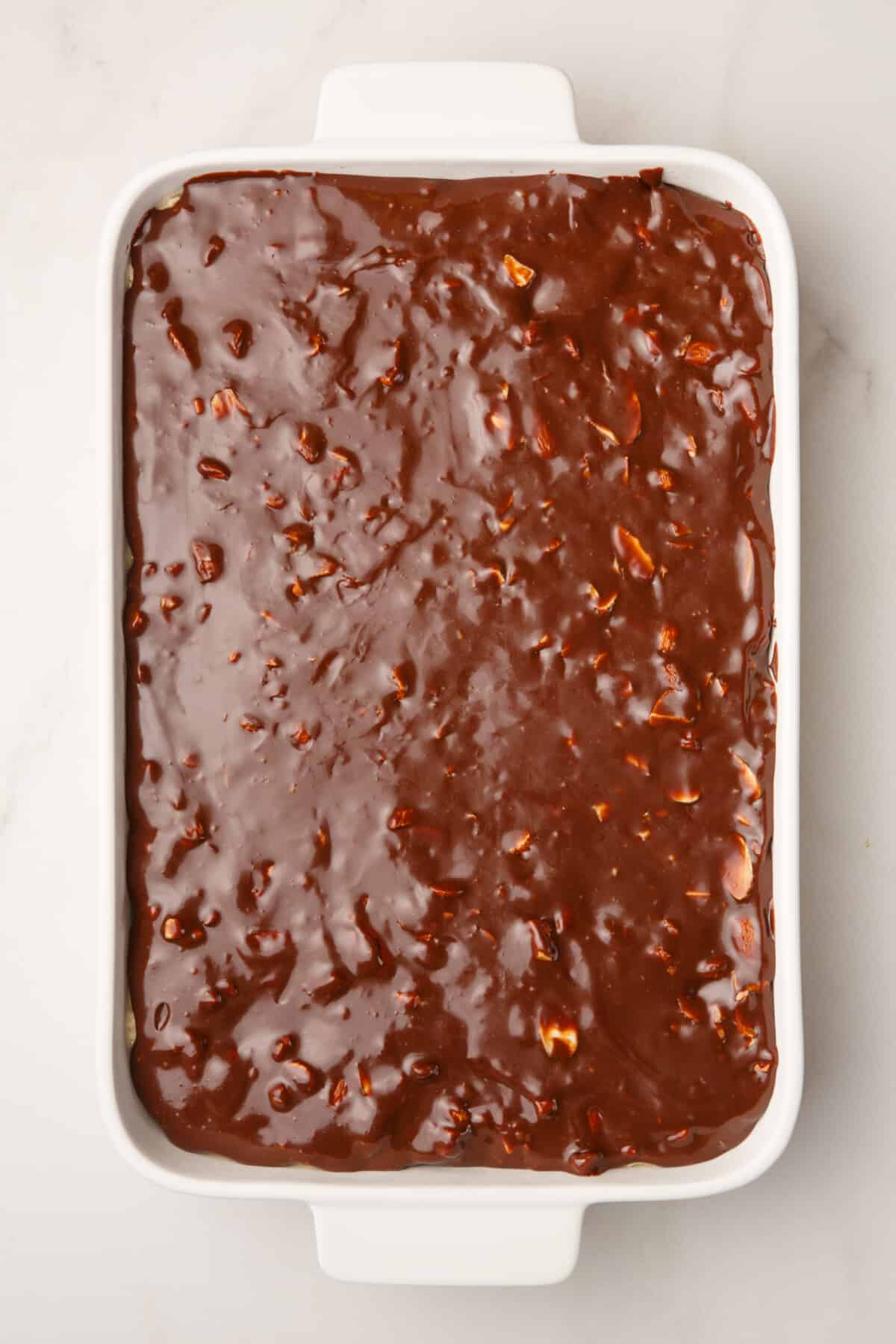 almond joy cake in a casserole dish topped with chocolate sauce and sliced almonds.