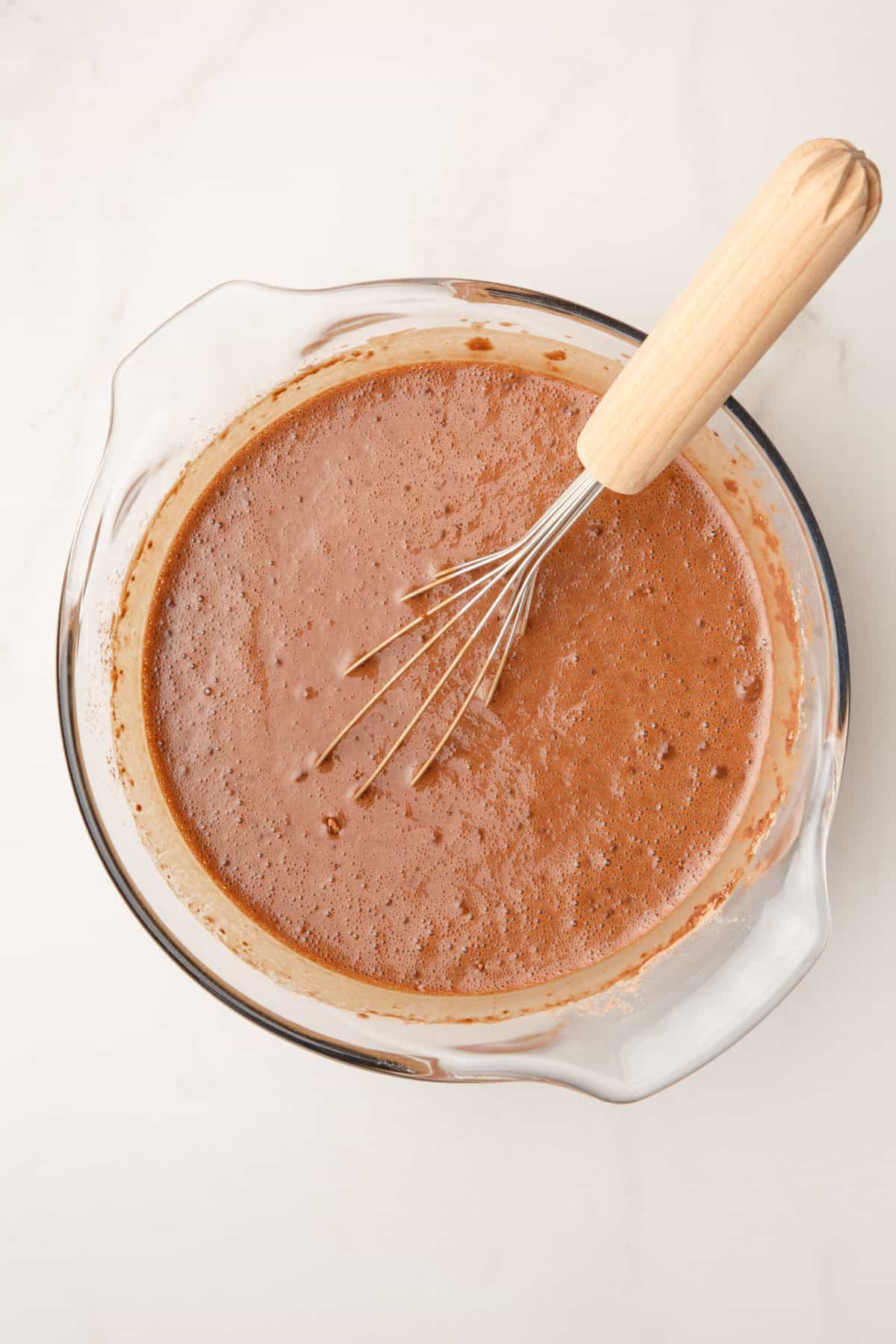 chocolate cake batter in a large glass bowl with a whisk