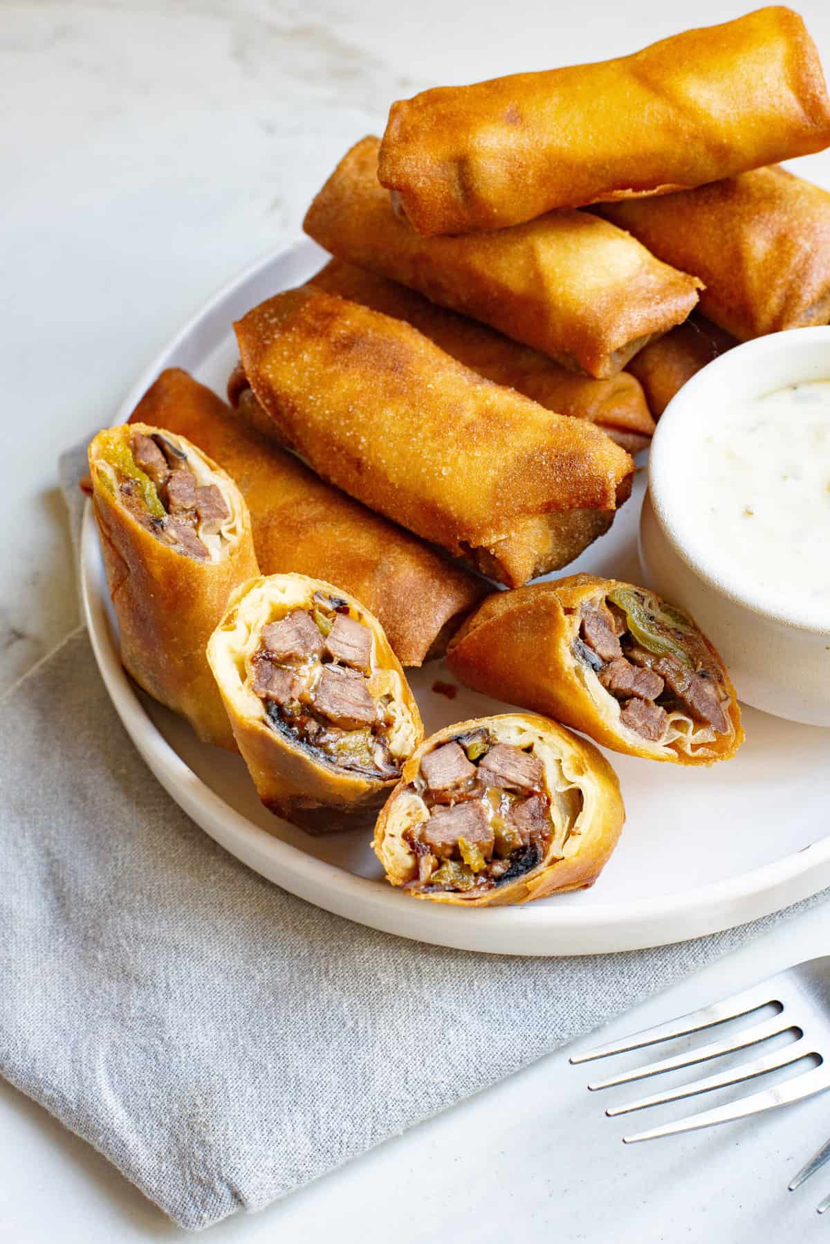 philly cheesesteak egg rolls some cut in half some not, all served on a white round plate