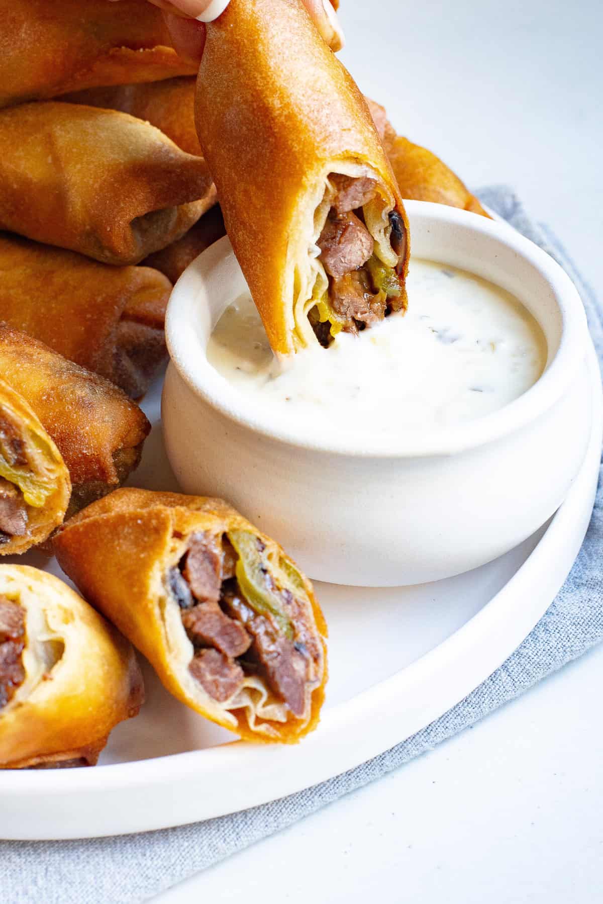 a philly cheesesteak egg rolls dipping into sauce