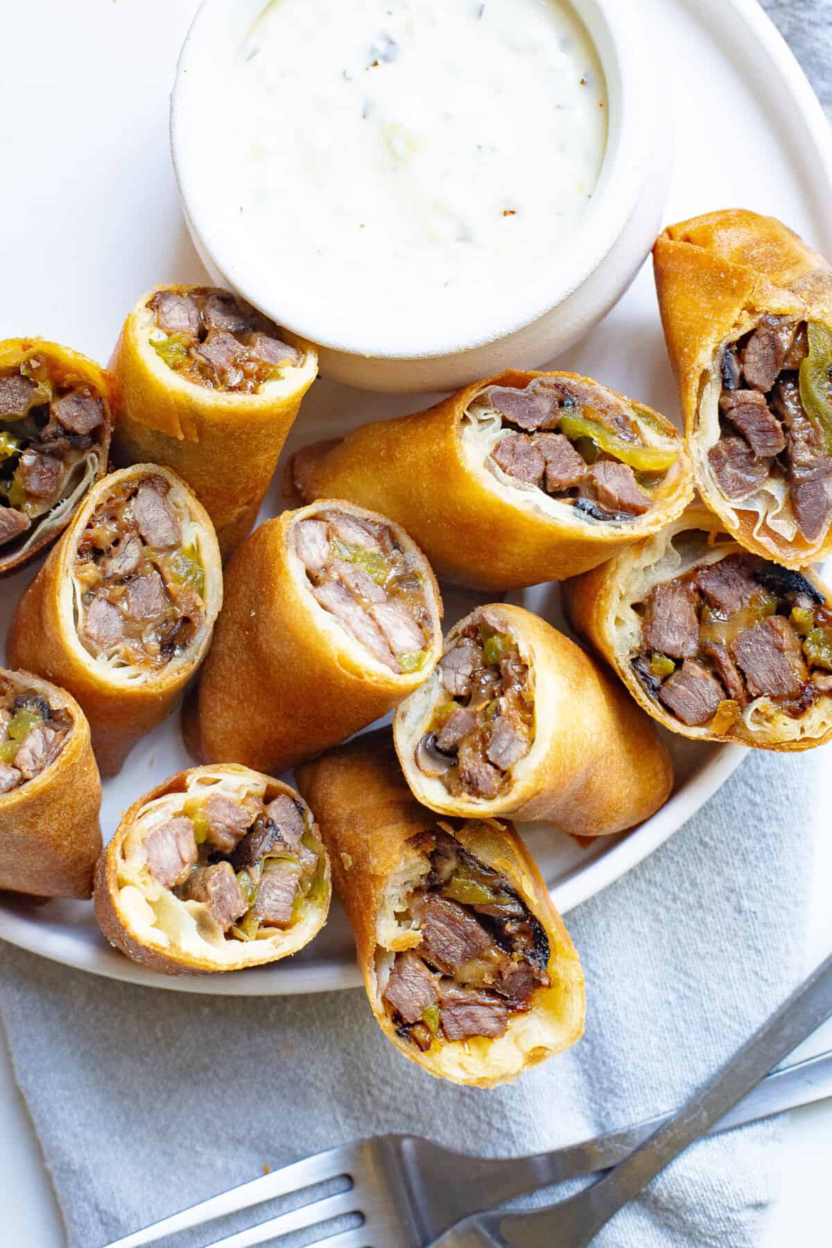 A basket of Philly Cheesesteak egg rolls with a bowl of dip. 