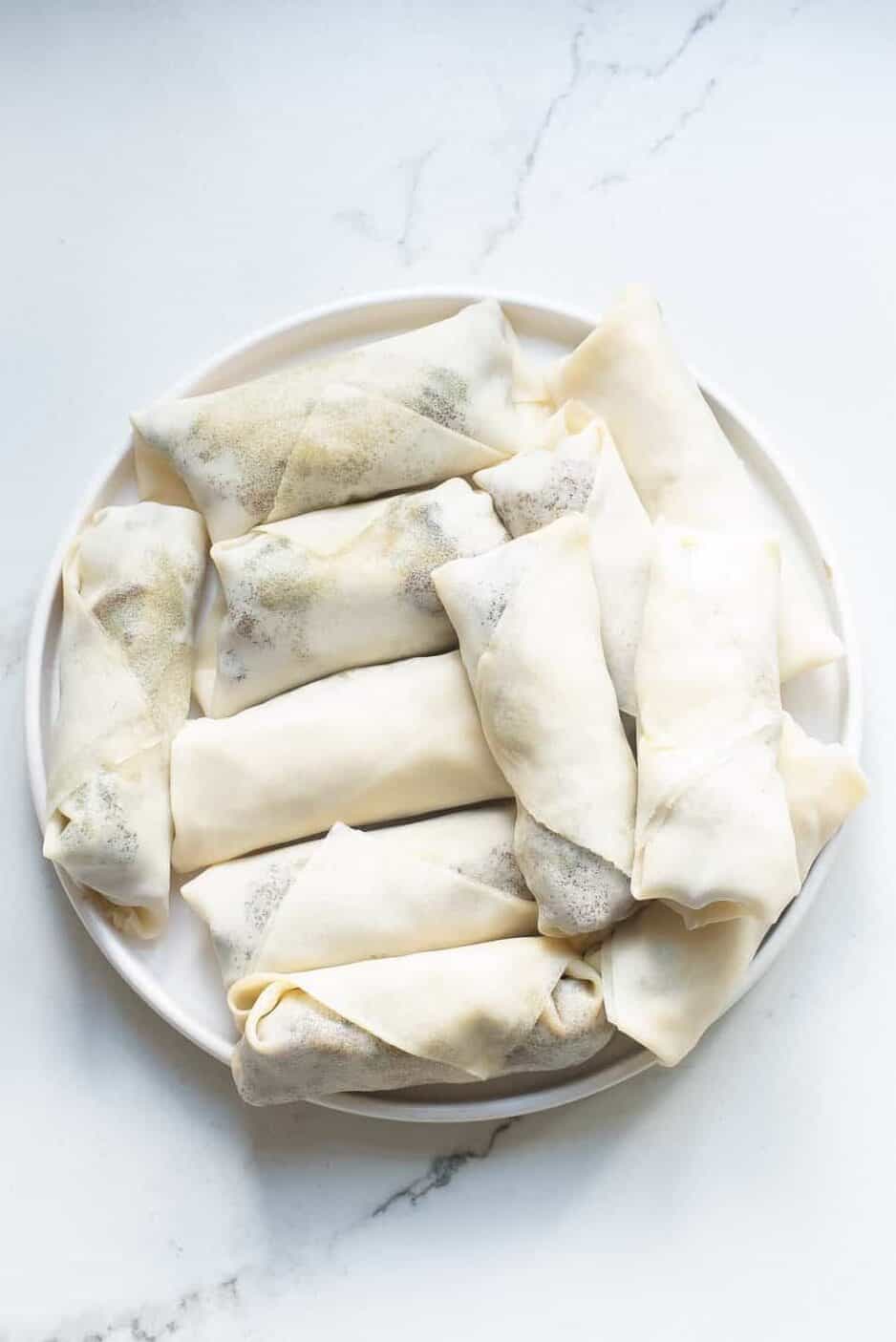 plate of wrapped and uncooked philly cheesesteak egg rolls