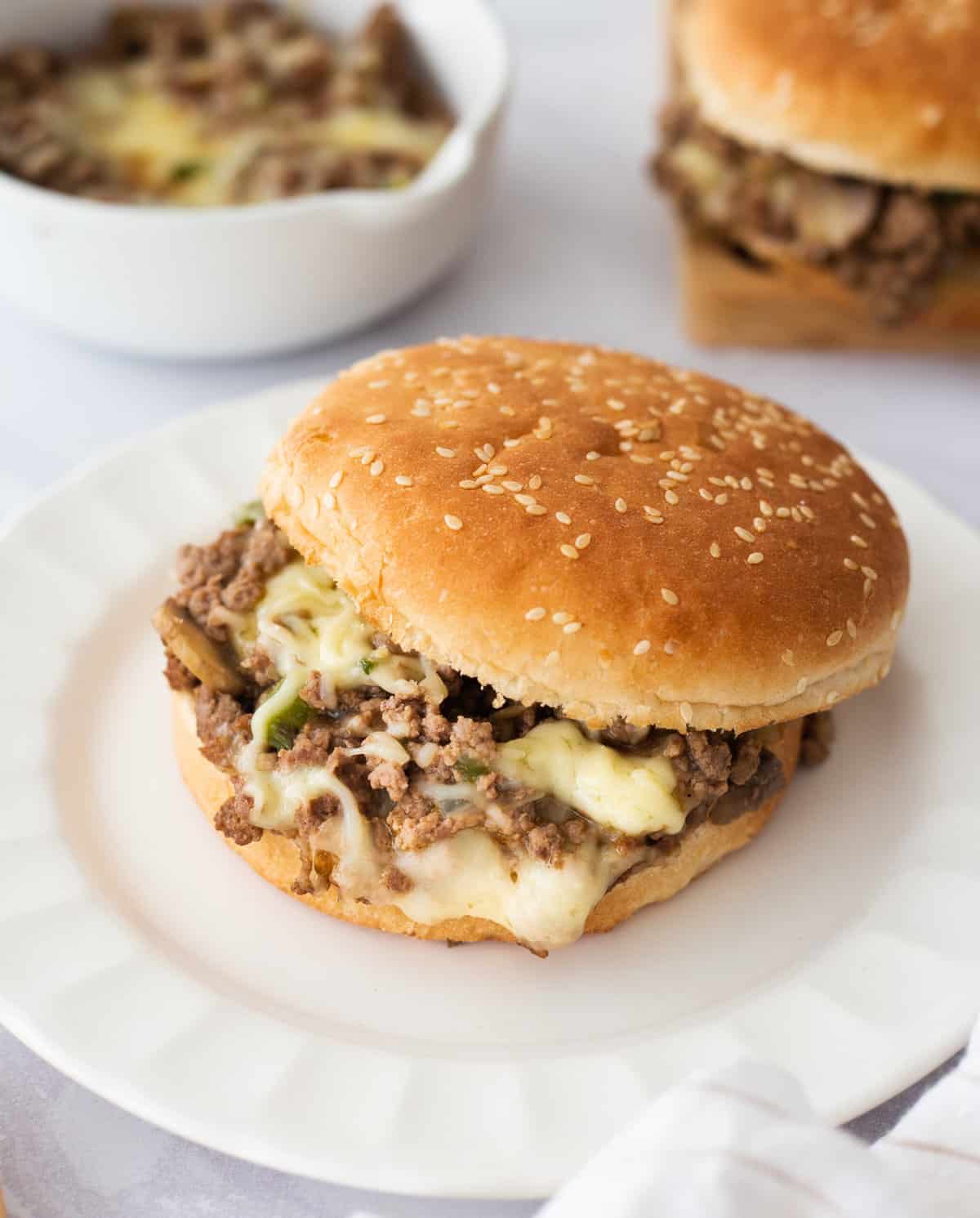 a plate with a philly cheesesteak sloppy joe sandwich sitting on a white round plate