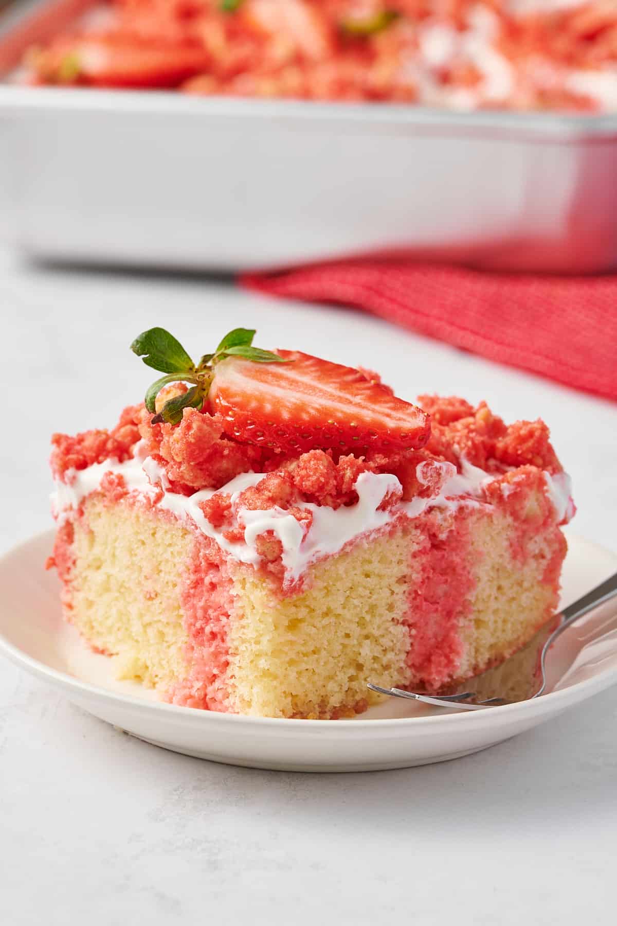 square slice serving of strawberry crunch poke cake served on a white round plate