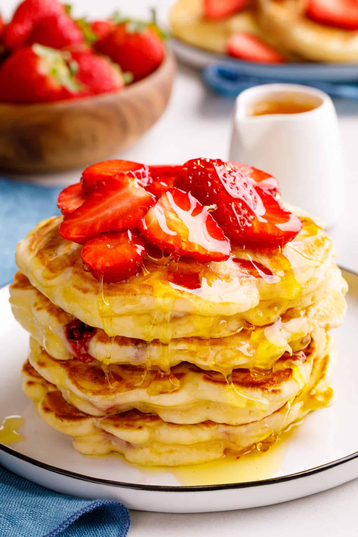 stack of four strawberry pancakes topped with fresh halved strawberries and syrup served on a white round plate