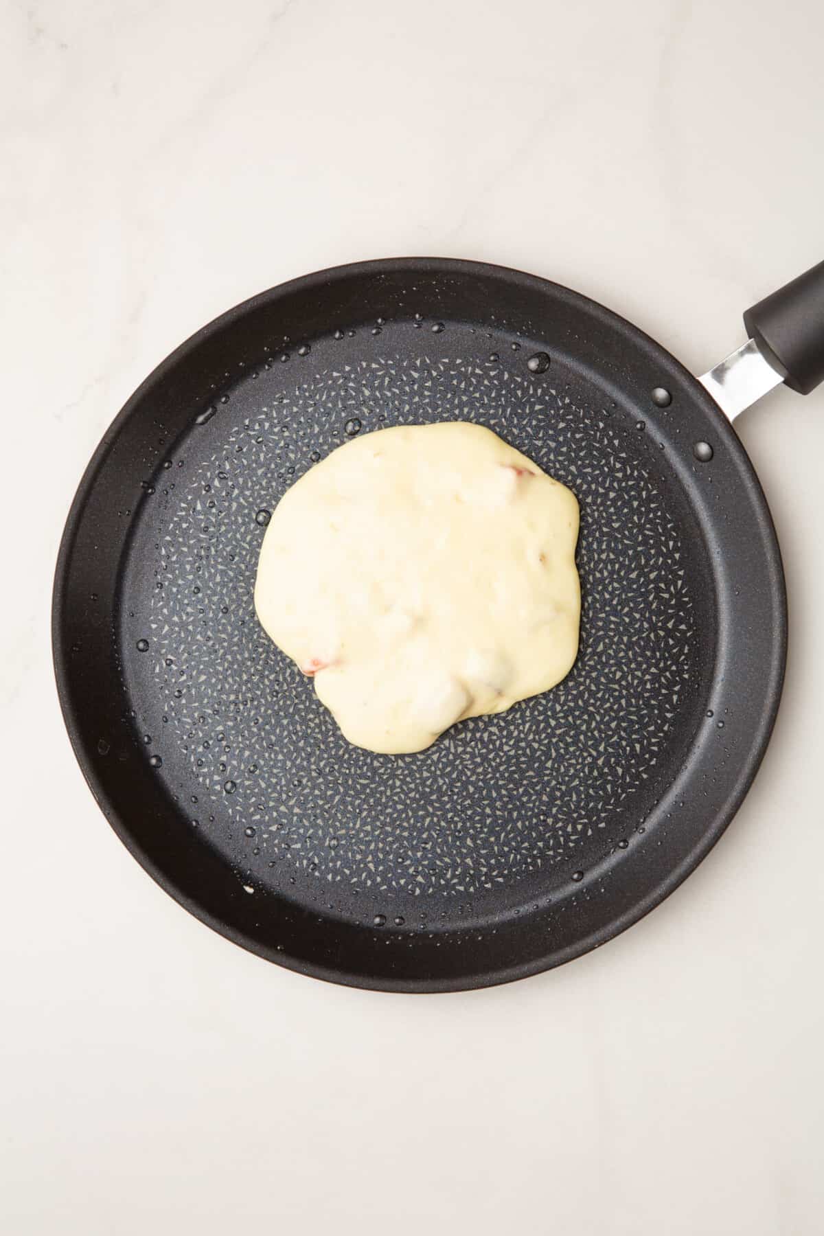 step 4 to make strawberry pancakes, ladle of strawberry pancakes cooking on a skillet pan.