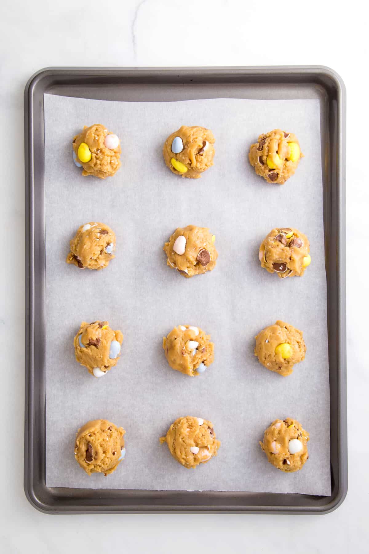 12 unbaked cadbury egg cookie dough arranged on a parchment lined baking sheet.