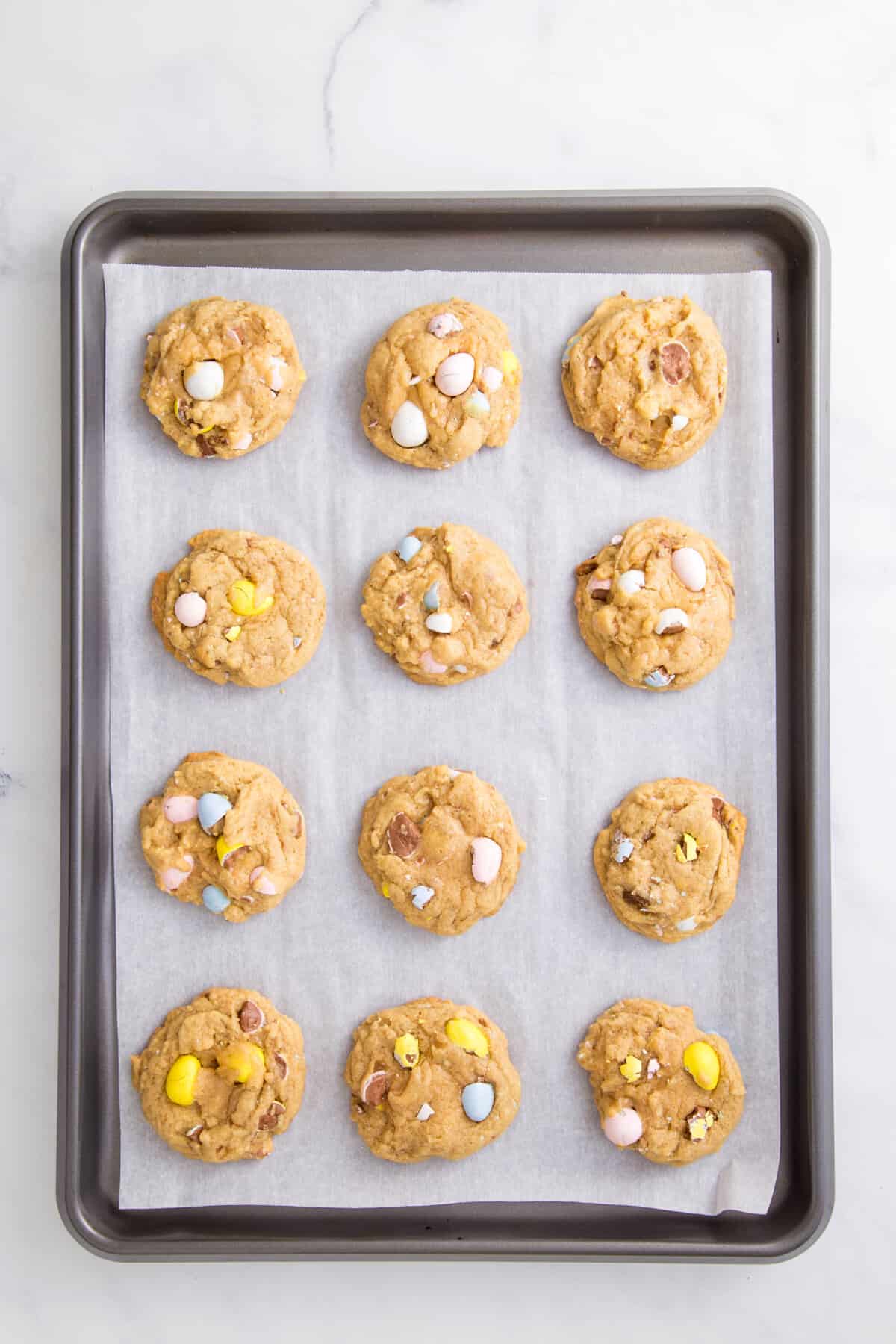 12 baked cadbury egg cookie dough arranged on a parchment lined baking sheet.